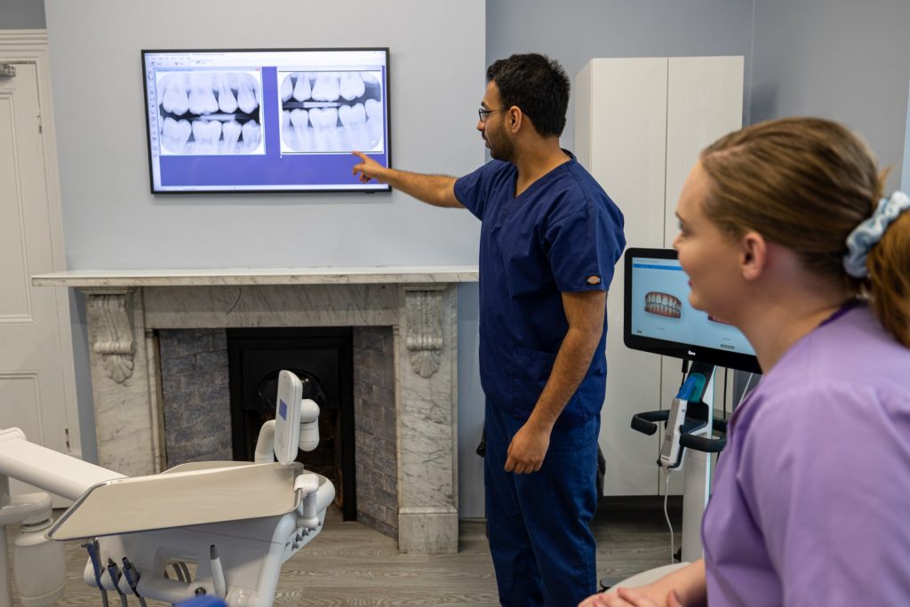 A dentist explaining a pair of x-rays on a wall screen to a colleague